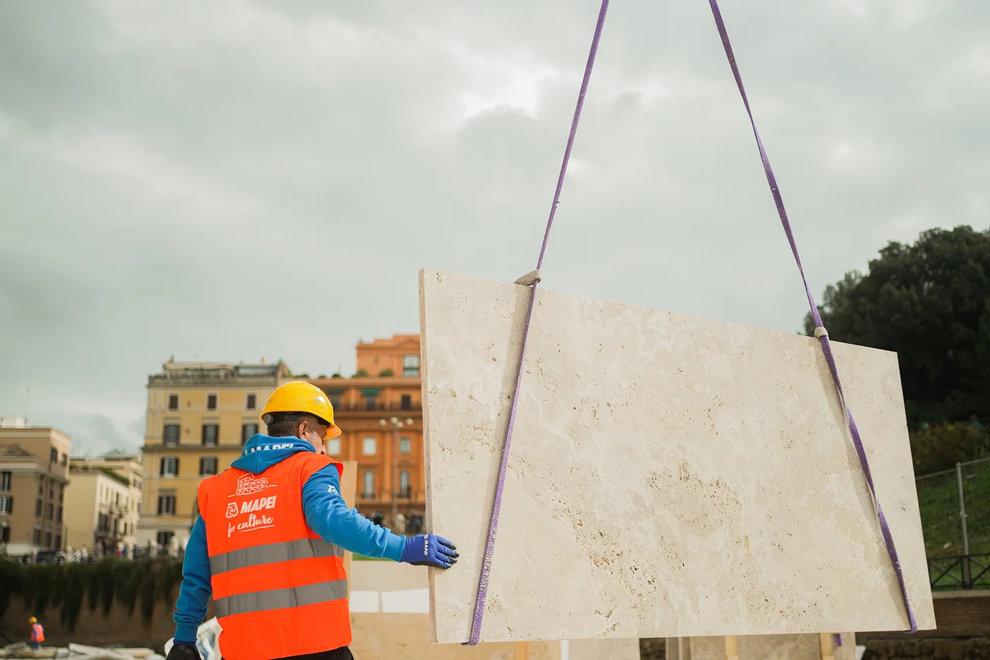 A worker guiding a large travertine slab into place on site, Rome’s skyline behind him