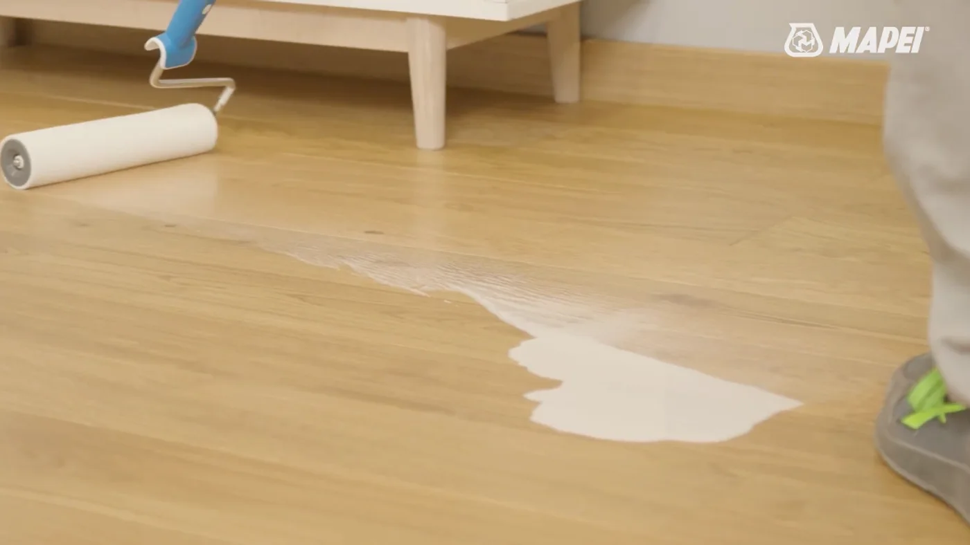 Close-up of the product being rolled onto a wooden floor, roller and applicator in frame