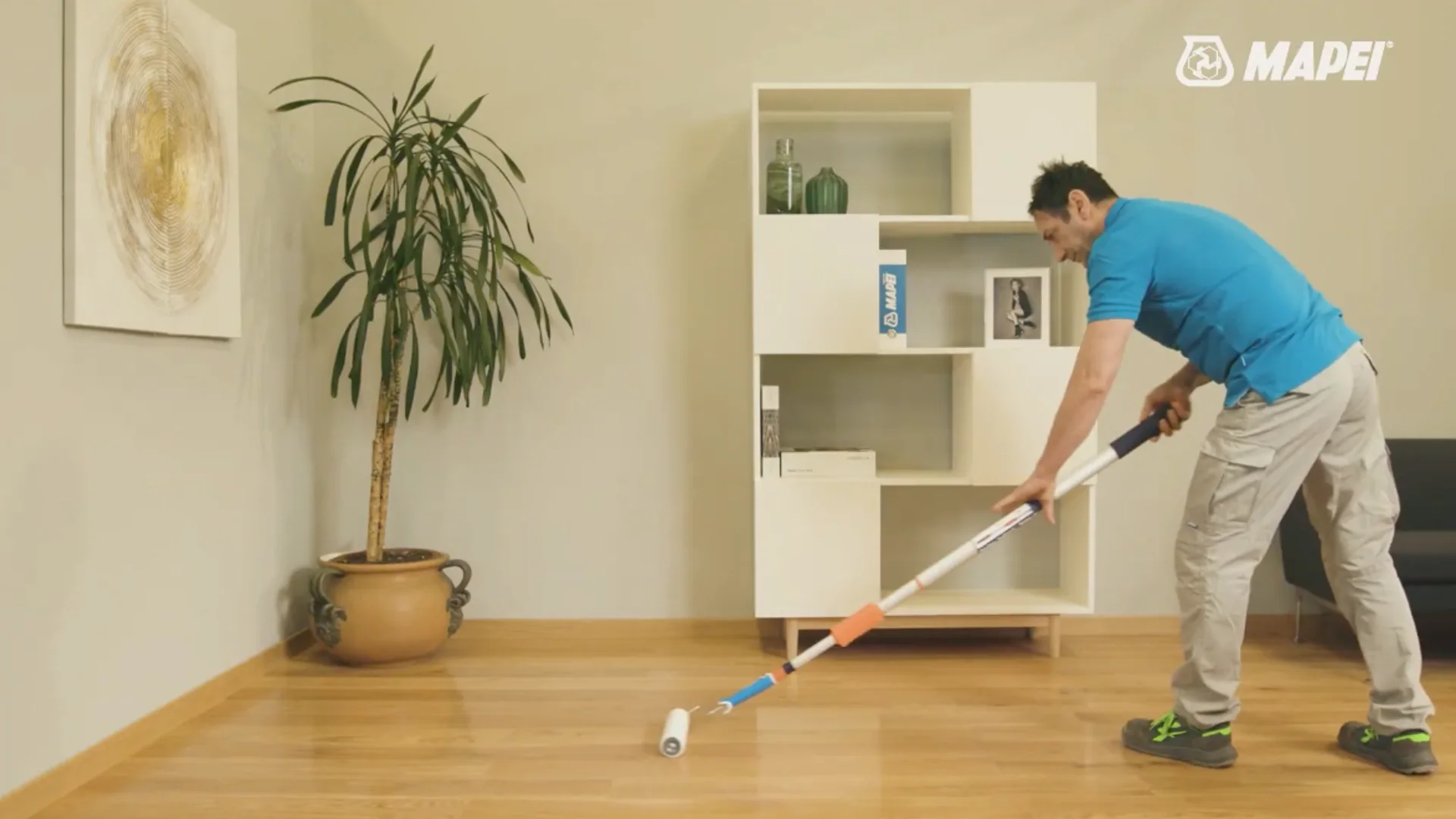 A man applying Mapei Ultracoat Renew FL to a wooden floor with a long-handled roller in a styled home interior