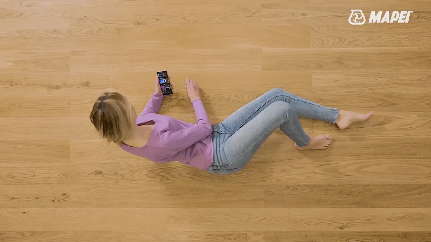 Overhead shot of a woman lying comfortably barefoot on the finished wooden floor, phone in hand